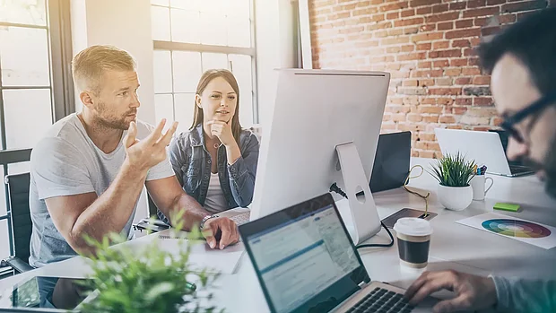 Beratungsteam arbeitet an einem großen Bildschirm und Laptops im modernen Büro an Strategien für nachhaltige Unternehmensentwicklung.