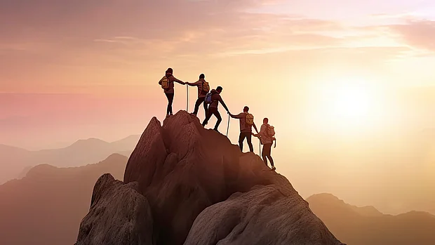 Menschen helfen sich gegenseitig beim Bergaufstieg auf einem felsigen Weg als Symbol für gemeinsames Vorankommen und unterstützende Beratung.